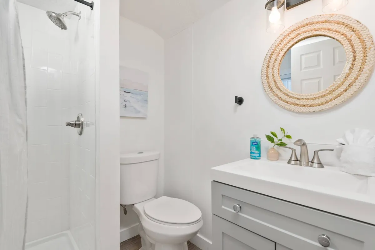A bright and modern private bathroom, showcasing a glass-enclosed shower, a sleek vanity with a sink, a decorative mirror, and soothing wall art. The space exudes both functionality and a calming ambiance, inviting refreshing personal care routines.