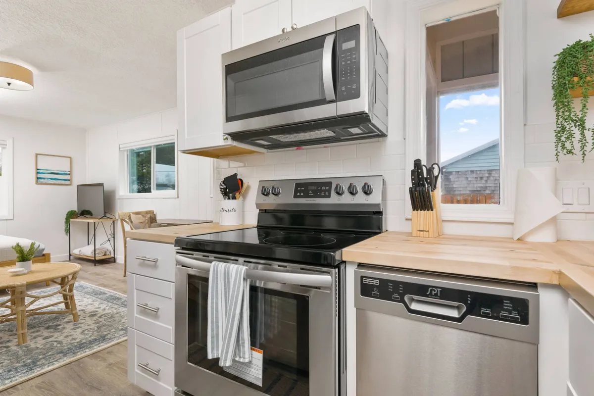 A cheerful and functional kitchen with stainless steel appliances, a butcher block countertop, and a large window letting in natural light. The open surfaces and easy-to-clean finishes are evident, making it practical for pet owners.