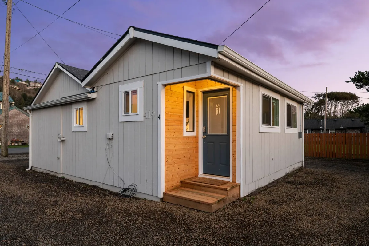 This exterior shot captures the front door of Coral Cottage, framed by wooden steps and gentle exterior lighting. The cozy porch invites guests to relax outside, and the overall atmosphere is warm and welcoming—perfect for arriving with a pet in tow. The cottage’s approachable facade and inviting entryway establish a sense of hospitality and comfort.