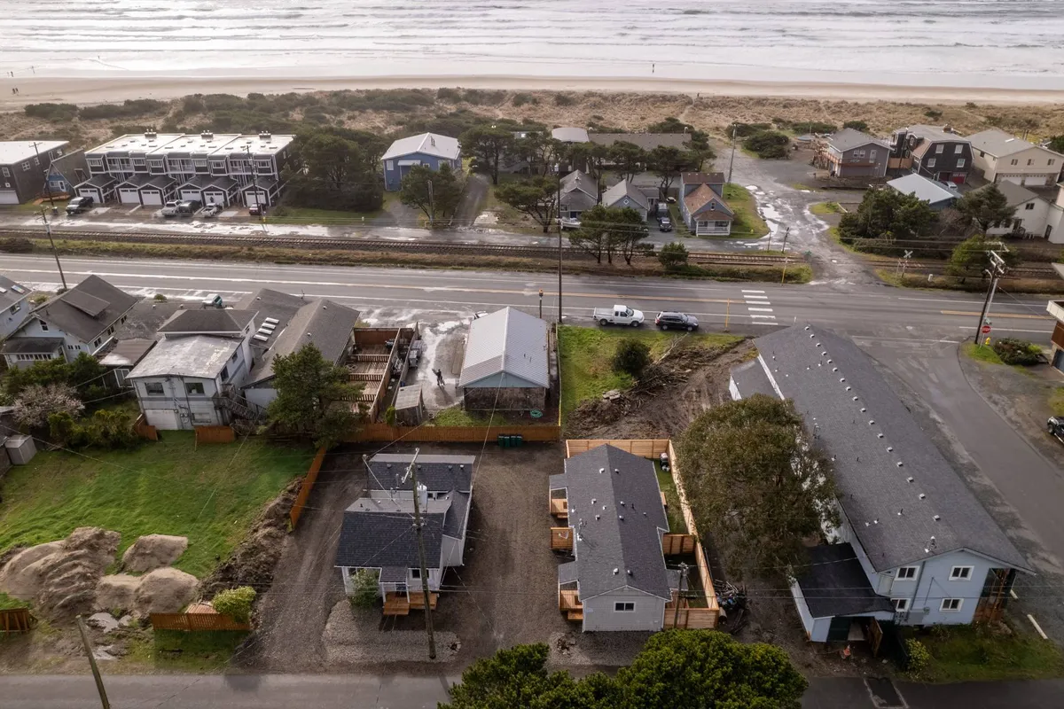 A broad ocean view framed by beachfront properties and the surrounding neighborhood. The shoreline stretches invitingly, with gentle waves and a tranquil atmosphere. The layout of the neighborhood and proximity to the beach are apparent, evoking a sense of easy access to both natural beauty and local amenities.